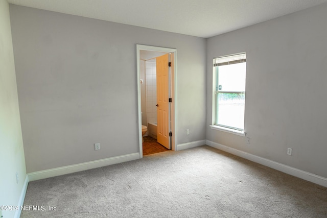 unfurnished bedroom with carpet floors, baseboards, and ensuite bathroom