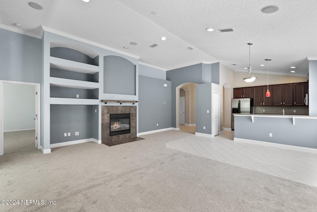 unfurnished living room featuring a textured ceiling, light colored carpet, crown molding, a tile fireplace, and built in features