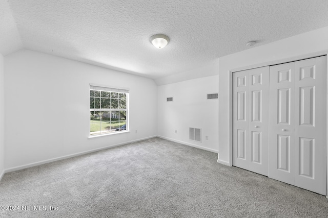 unfurnished bedroom featuring a textured ceiling, light carpet, a closet, and vaulted ceiling