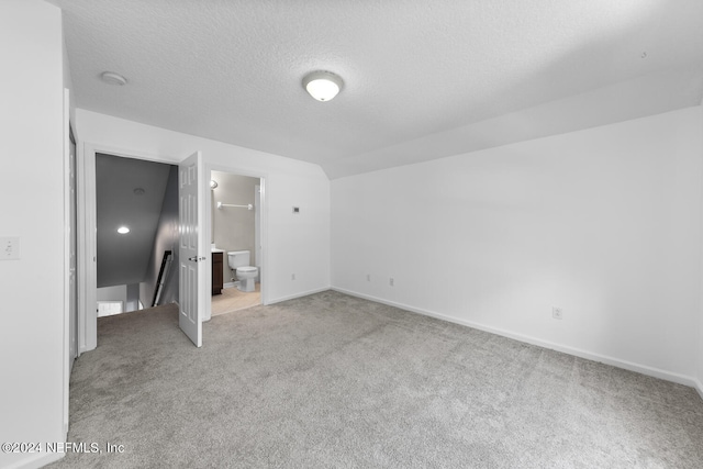 unfurnished bedroom featuring a walk in closet, connected bathroom, light colored carpet, and vaulted ceiling