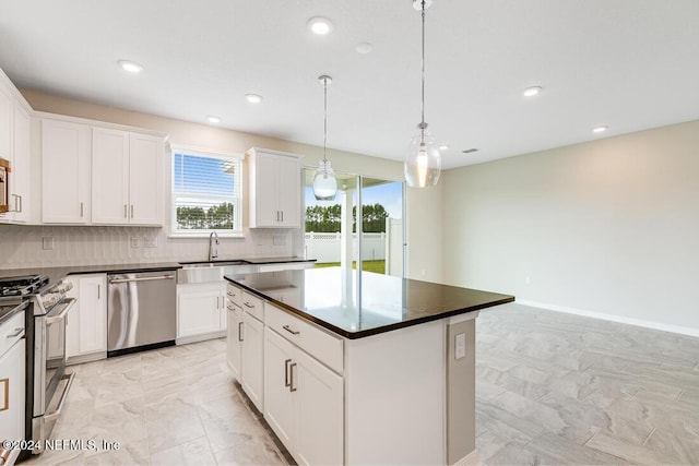 kitchen with white cabinets, sink, appliances with stainless steel finishes, decorative light fixtures, and a kitchen island