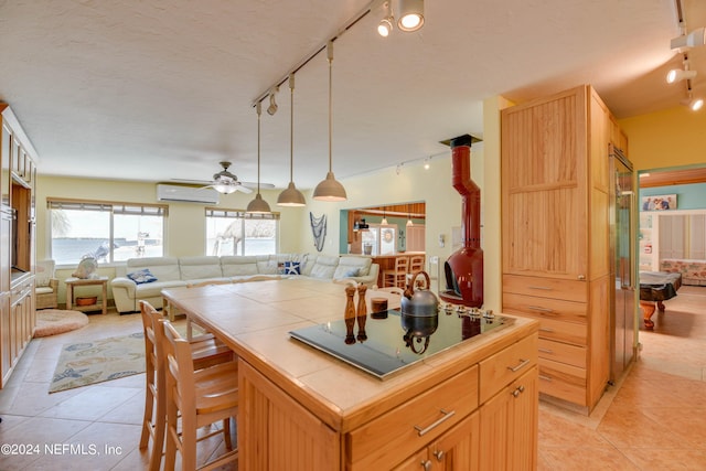 kitchen featuring black electric stovetop, light tile patterned floors, a kitchen island, a wall mounted AC, and tile counters