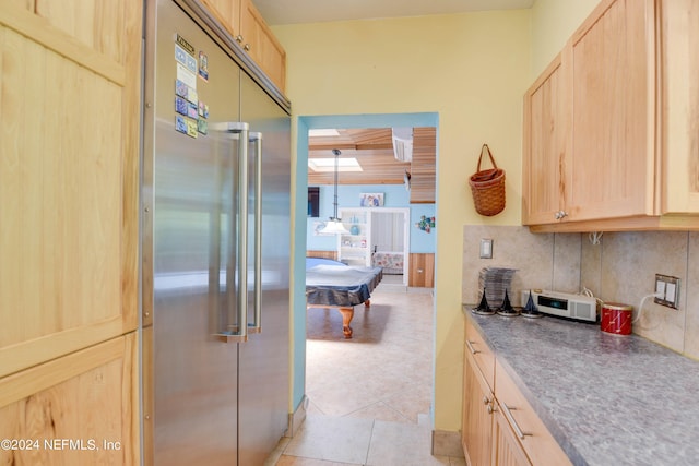 kitchen featuring light brown cabinetry, light tile patterned flooring, high end fridge, and tasteful backsplash