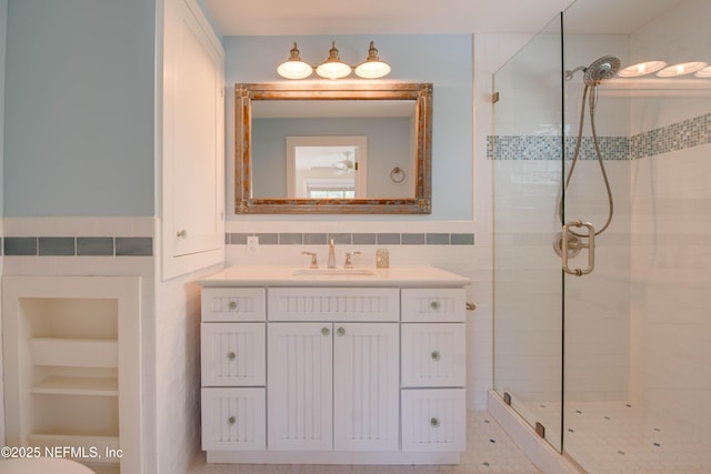 bathroom with a shower with shower door, tile walls, and vanity