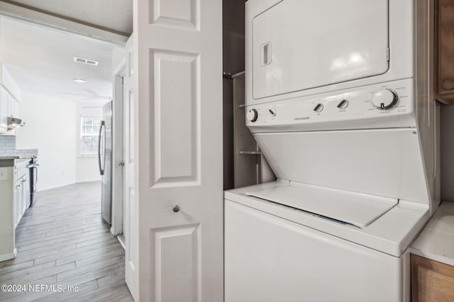 washroom featuring visible vents, stacked washer and clothes dryer, laundry area, and light wood-type flooring