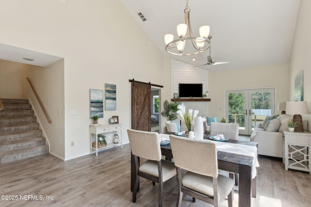 dining room featuring stairway, visible vents, light wood finished floors, high vaulted ceiling, and a barn door