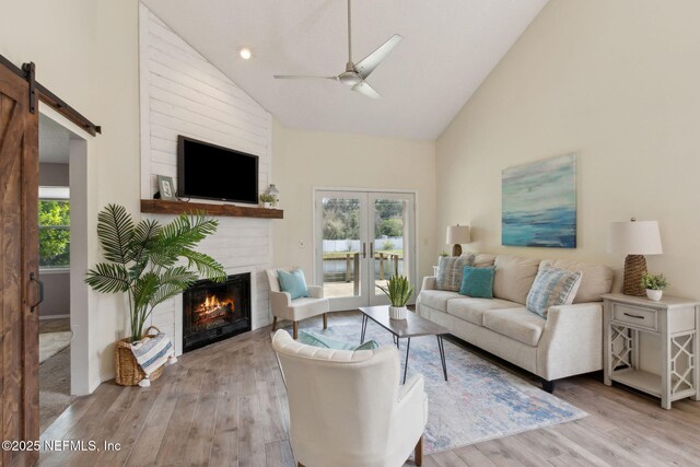 living room featuring a barn door, high vaulted ceiling, wood finished floors, and a fireplace