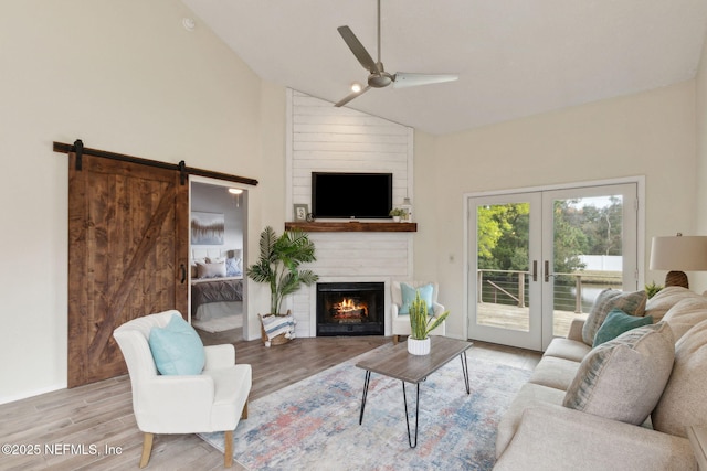 living room with a ceiling fan, wood finished floors, a barn door, a large fireplace, and french doors