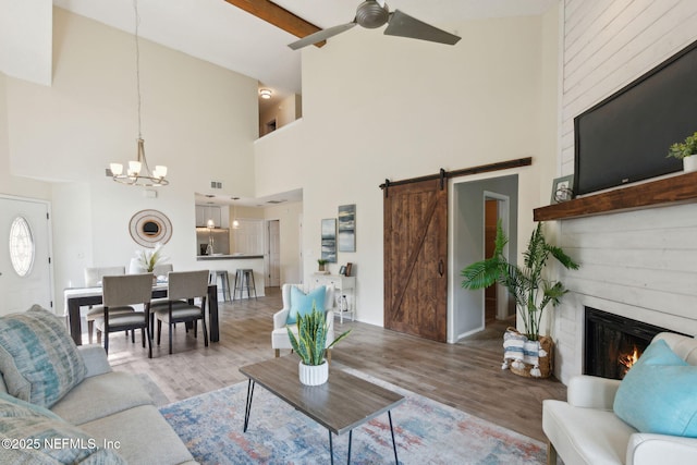 living room with ceiling fan with notable chandelier, a fireplace, a barn door, and wood finished floors