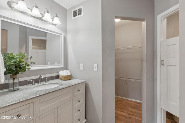 bathroom featuring vanity, a walk in closet, wood finished floors, and visible vents