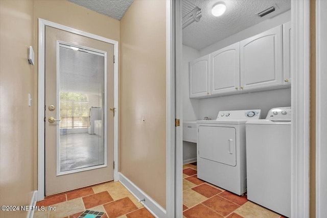 clothes washing area with washer and clothes dryer, cabinets, and a textured ceiling