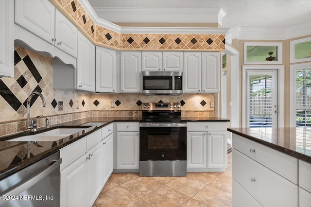 kitchen featuring white cabinetry, sink, dark stone countertops, appliances with stainless steel finishes, and ornamental molding