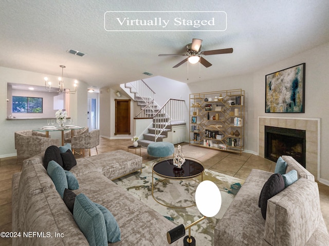 tiled living room with ceiling fan with notable chandelier, a tile fireplace, and a textured ceiling