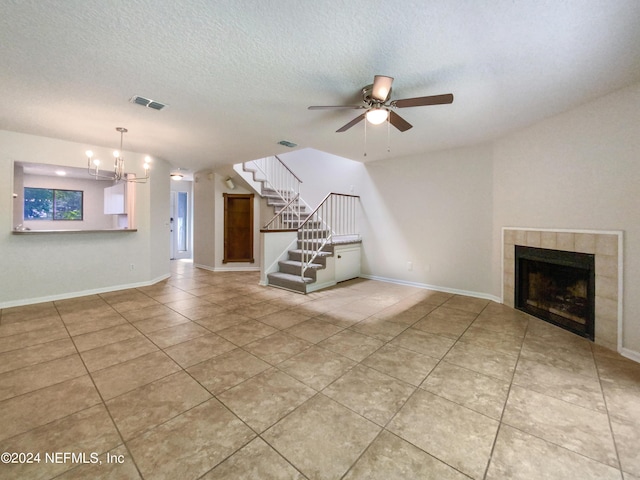 unfurnished living room featuring ceiling fan with notable chandelier, a tile fireplace, a textured ceiling, and light tile patterned floors