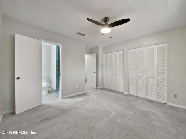 unfurnished bedroom featuring ceiling fan, multiple closets, light carpet, and ensuite bath