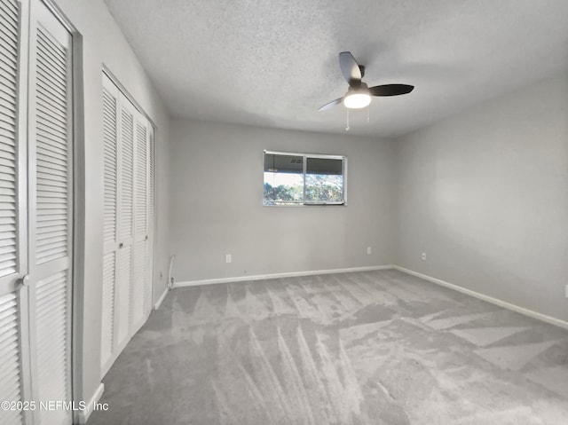 unfurnished bedroom with light carpet, a textured ceiling, ceiling fan, and multiple closets