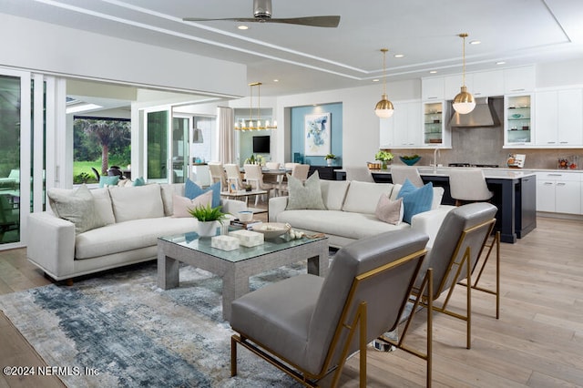 living room with sink, ceiling fan with notable chandelier, and light hardwood / wood-style flooring