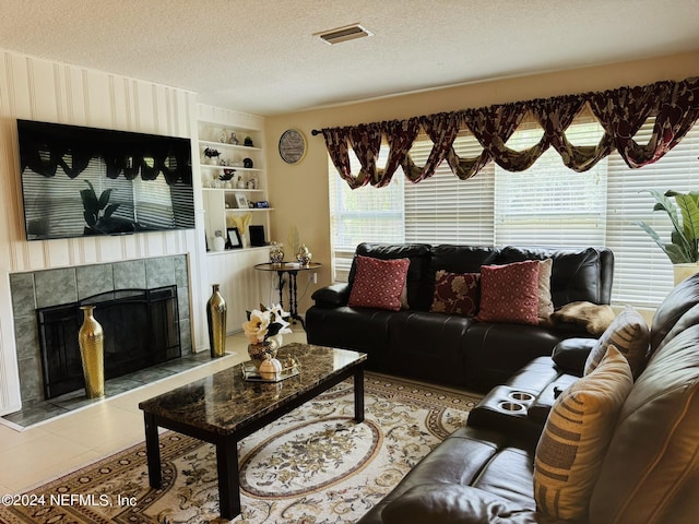 living room with light tile patterned flooring, built in shelves, a textured ceiling, and a tiled fireplace