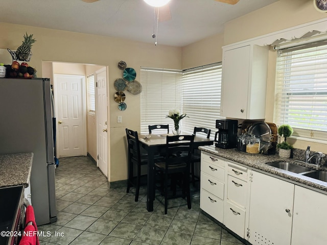 kitchen with stainless steel fridge, white cabinetry, sink, and light tile patterned flooring