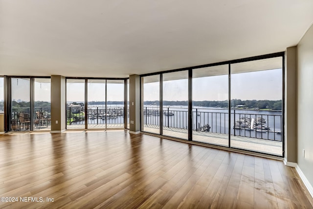 spare room featuring wood-type flooring, a water view, a wealth of natural light, and expansive windows