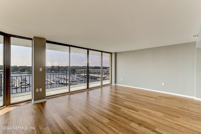 empty room with light wood-type flooring, a water view, and floor to ceiling windows