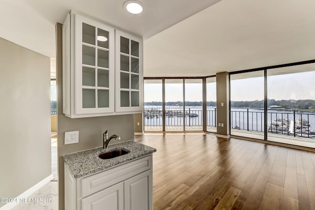 interior space with white cabinetry, sink, light stone countertops, expansive windows, and a water view