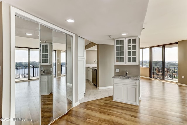 kitchen featuring dishwasher, sink, white cabinets, light stone counters, and a water view