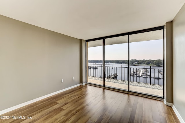 empty room featuring expansive windows, hardwood / wood-style floors, and a water view