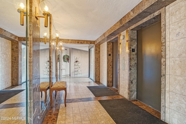 hall featuring elevator, tile walls, a textured ceiling, and an inviting chandelier