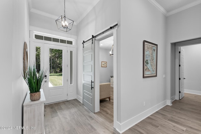 entrance foyer with a notable chandelier, a barn door, ornamental molding, and light hardwood / wood-style flooring