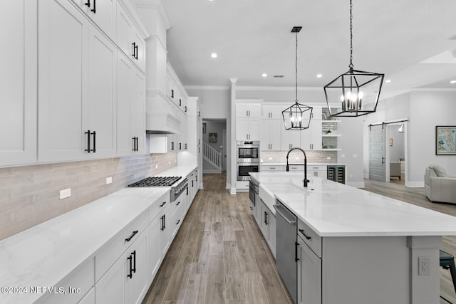 kitchen with a barn door, a spacious island, pendant lighting, white cabinets, and appliances with stainless steel finishes