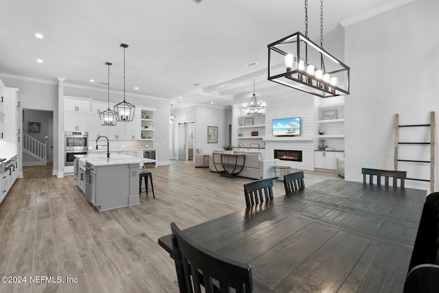 dining space featuring a large fireplace, light hardwood / wood-style flooring, ornamental molding, and sink