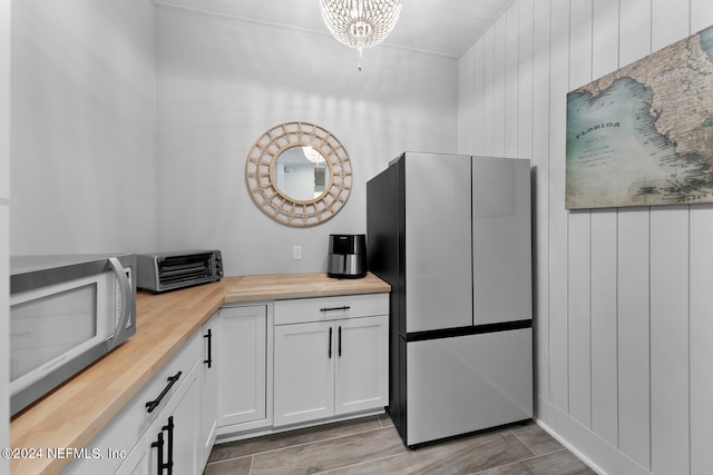 kitchen with wooden counters, stainless steel fridge, wood walls, a chandelier, and white cabinets