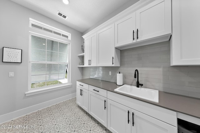 kitchen with sink, light tile patterned floors, tasteful backsplash, a textured ceiling, and white cabinets