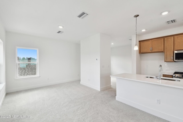 kitchen with a sink, visible vents, light countertops, brown cabinets, and pendant lighting