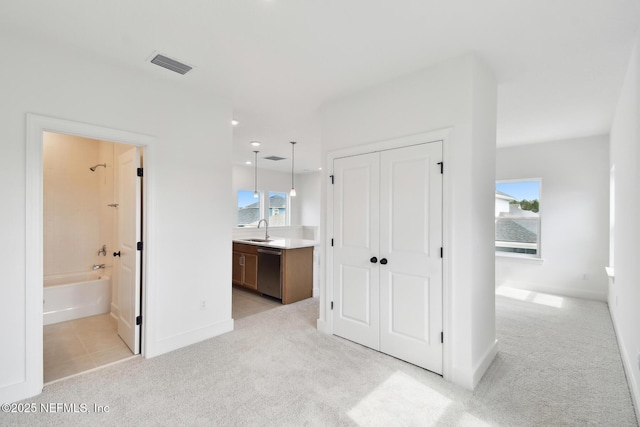 unfurnished bedroom featuring a closet, light colored carpet, visible vents, a sink, and ensuite bath