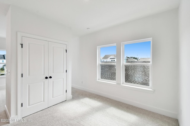 unfurnished bedroom with baseboards, a closet, and light colored carpet