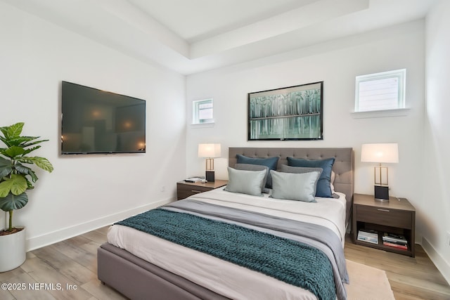 bedroom with a tray ceiling, light wood-type flooring, and baseboards