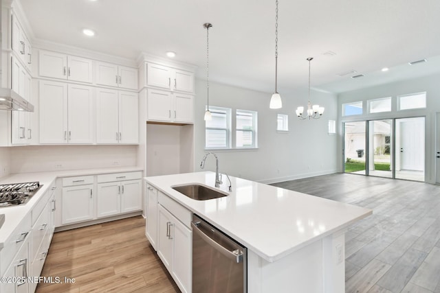 kitchen with a kitchen island with sink, stainless steel appliances, a sink, hanging light fixtures, and light countertops