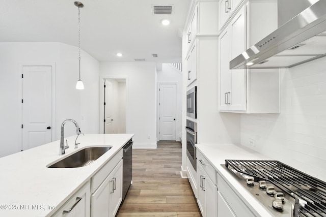 kitchen with a sink, white cabinetry, light countertops, wall chimney range hood, and pendant lighting