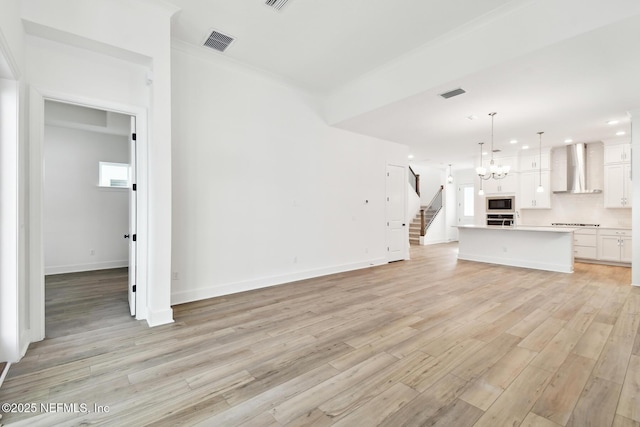 unfurnished living room with light wood-style flooring, visible vents, a chandelier, and baseboards