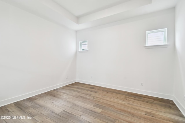 unfurnished room featuring light wood finished floors, baseboards, and a tray ceiling