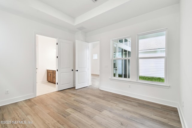 unfurnished room with light wood-type flooring, a raised ceiling, visible vents, and baseboards