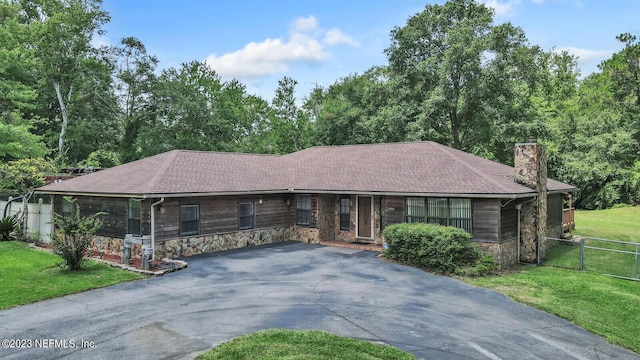 ranch-style home with stone siding, a chimney, aphalt driveway, fence, and a front lawn