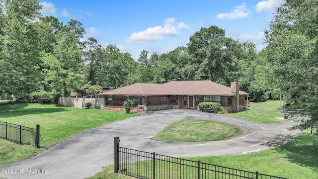 ranch-style house with driveway, a chimney, fence, and a front lawn