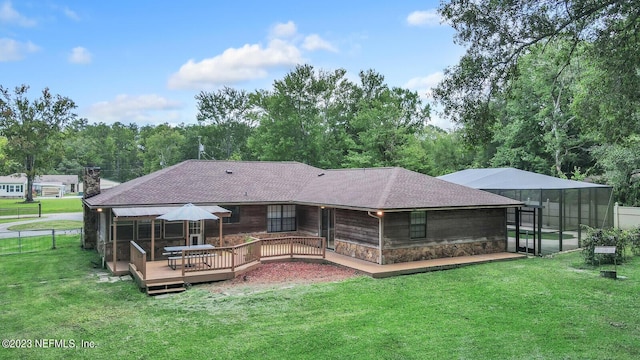 back of house with a yard, a shingled roof, a deck, stone siding, and a lanai
