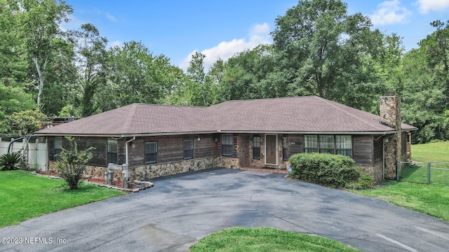 single story home with aphalt driveway, roof with shingles, a chimney, fence, and a front lawn