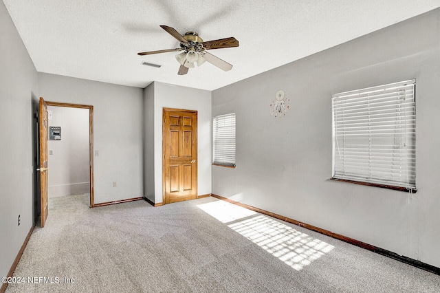 unfurnished bedroom featuring a textured ceiling, carpet floors, a ceiling fan, visible vents, and baseboards