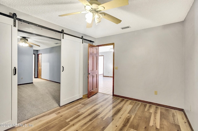 empty room with light wood finished floors, a barn door, ceiling fan, a textured ceiling, and baseboards