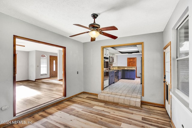 empty room with light wood-style floors, a ceiling fan, baseboards, and a textured ceiling